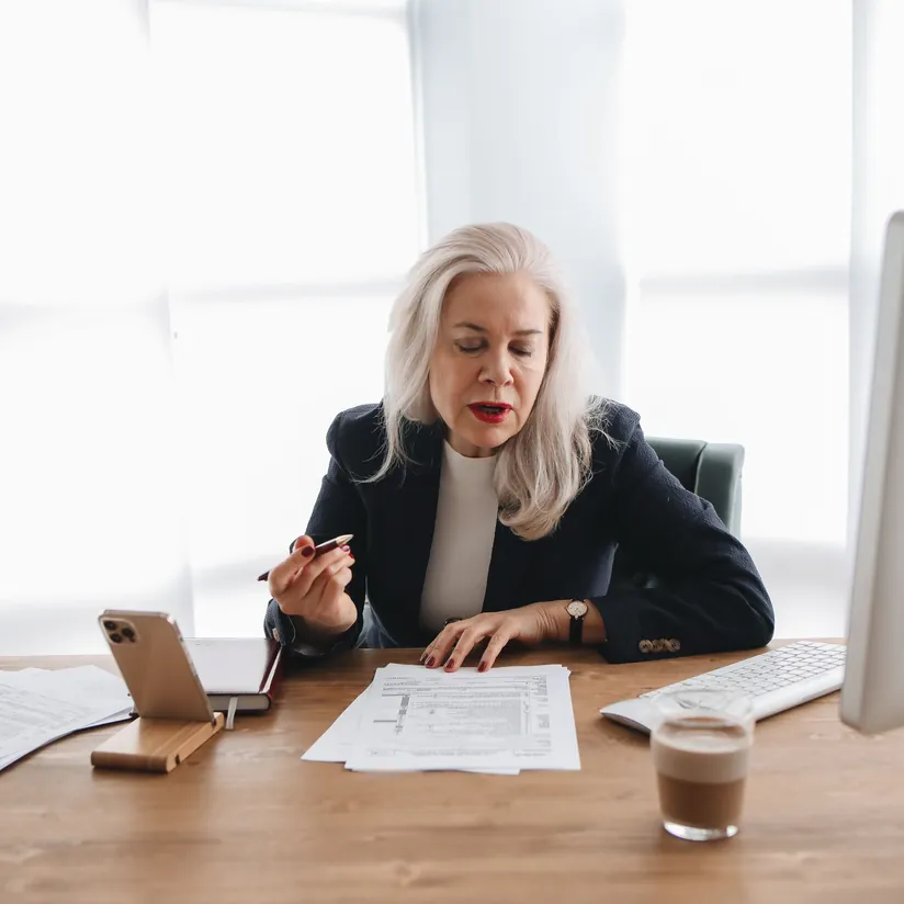 Finance executive reviewing printed financial forms at a desk with a phone, keyboard and coffee