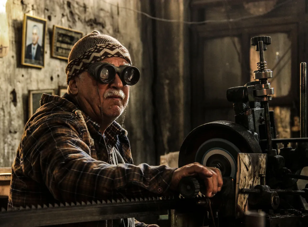 Elderly man in a workshop wearing goggles operates machinery