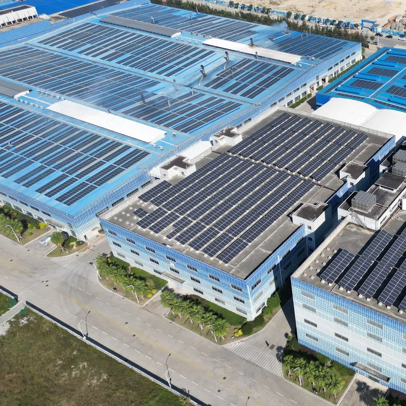 Aerial view of factory buildings with solar panels covering their roofs beside an empty road