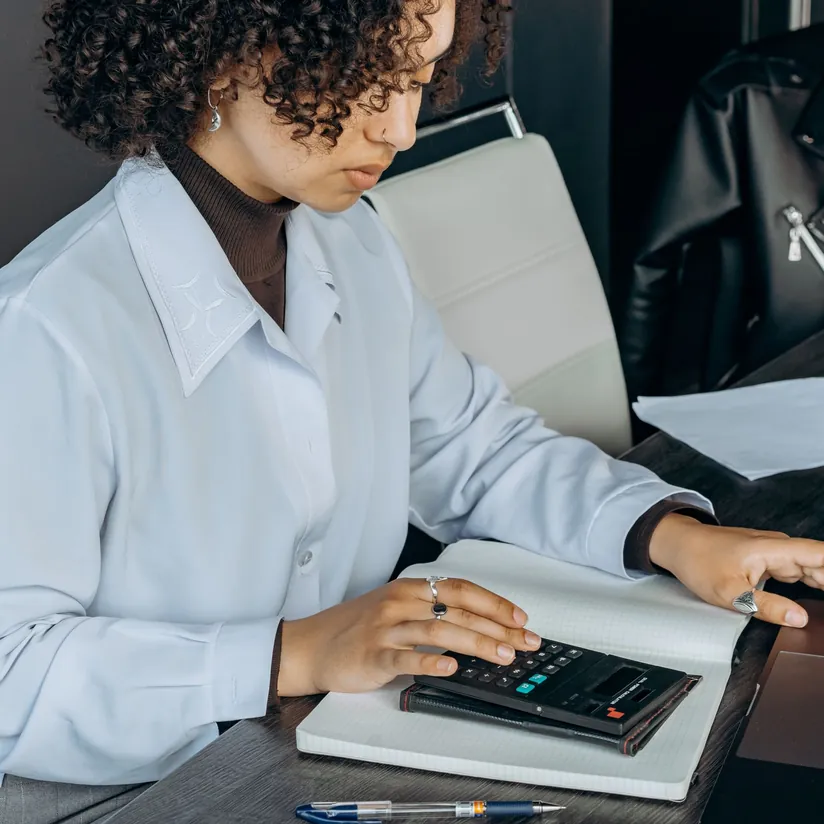 Professional using a calculator over an open notebook at an office desk