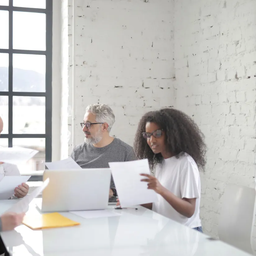 Colleagues reviewing printed documents around a laptop at a conference table in a bright office