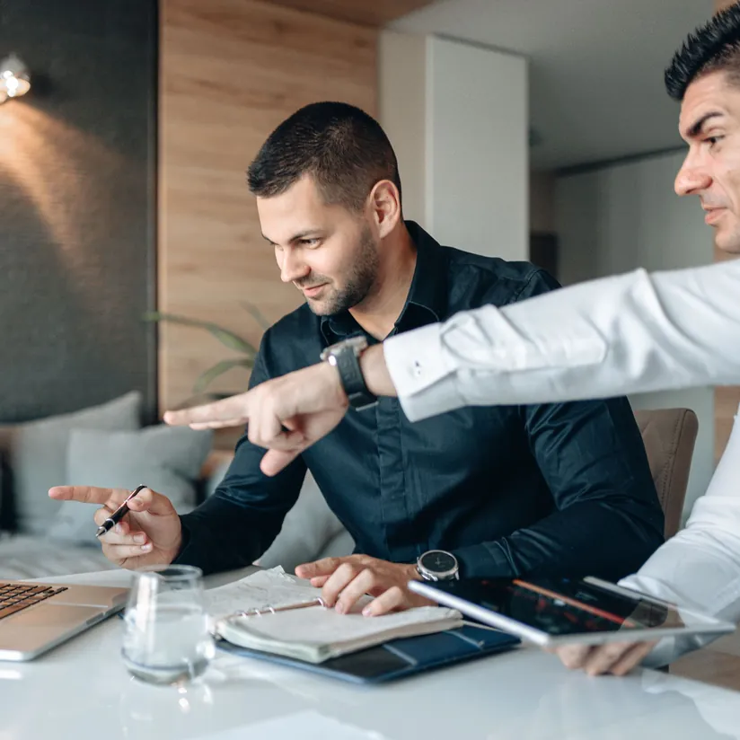 Two business colleagues reviewing a laptop and tablet at a table, one pointing at the screen