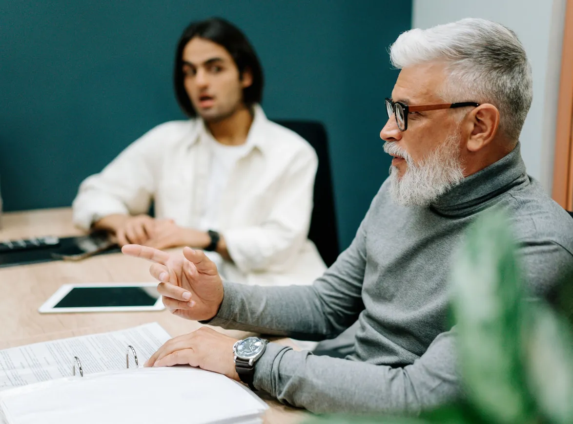 Senior professional gesturing while collaborating with colleague in a modern office