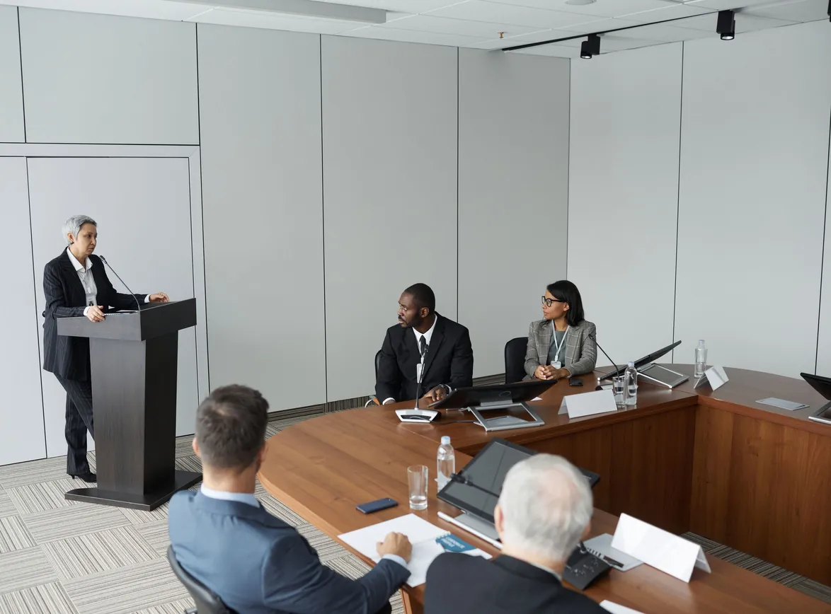 Group of professionals in a formal meeting setting with a speaker at the podium