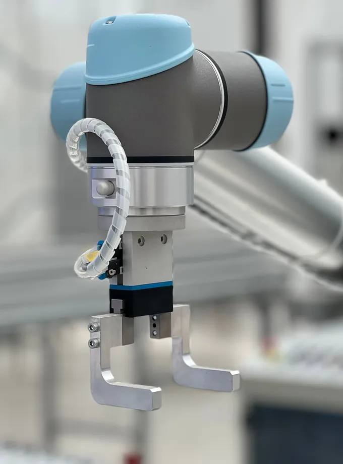 Blue and gray collaborative robot arm with a two-finger metal gripper in a blurred industrial workspace